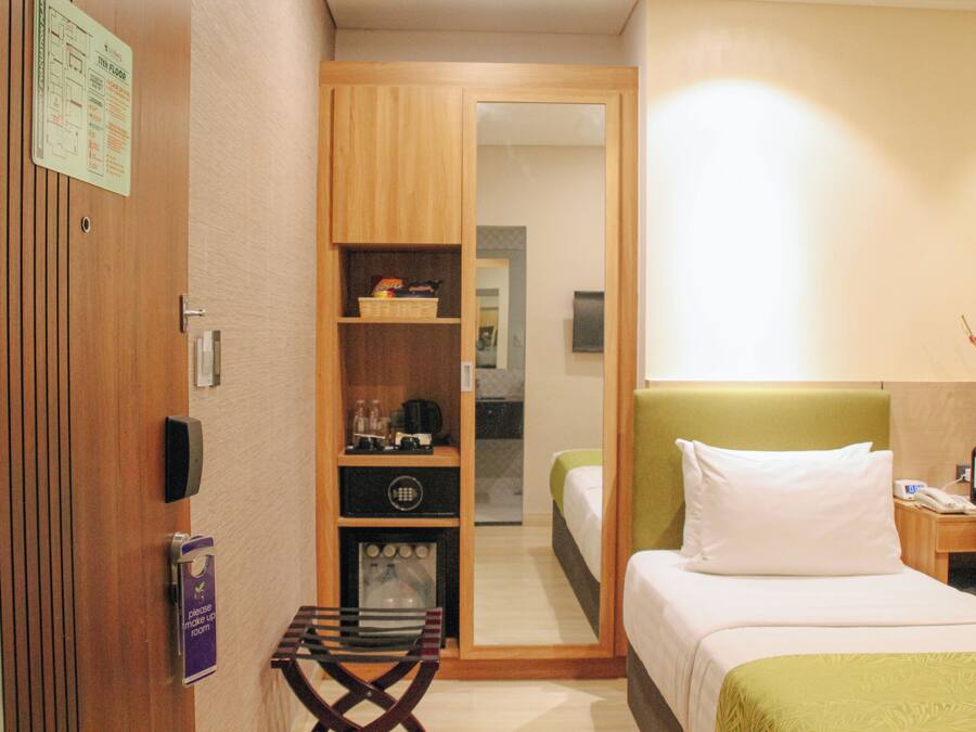 Een hotelkamer met een bed, een tafeltje, een plank met spullen en een spiegel.