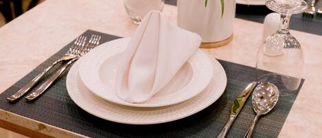 A dining table set with plates, cutlery, napkins, and a potted plant.