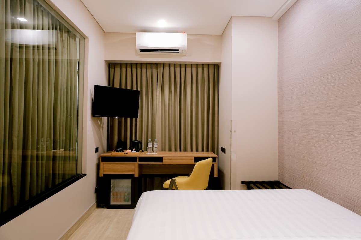 A hotel room with a bed, a desk with a chair, a television, and an air conditioning unit.