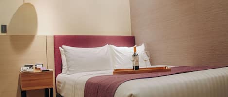 A neatly made bed with a wooden nightstand beside it, a bottle of wine, and a tray with glasses on the nightstand.