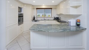 Cozinha moderna com armários brancos, bancada de granito e janela com plantas em vasos.