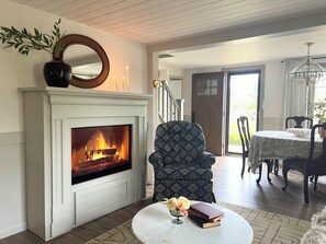 A living room with a fireplace, a patterned armchair, a dining area with a table and chairs, and a view of the outdoors. - VINTAGE VIBES - HOT TUB - KING BED - COTTAGE ABODE (State College)