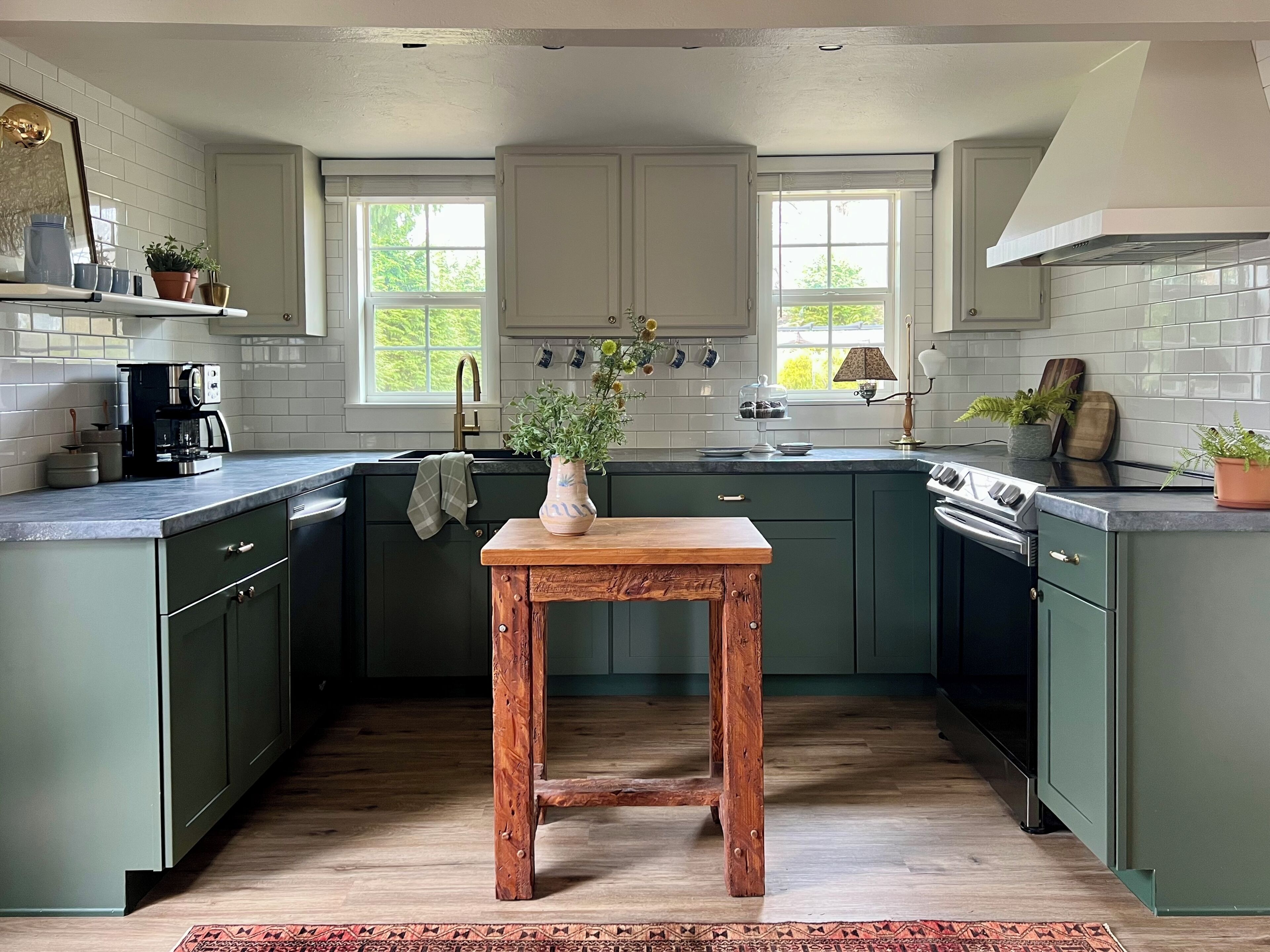 A kitchen with green cabinets, a wooden table, and a coffee machine.