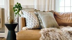 Un salon chaleureux avec un canapé en cuir marron, des coussins à motifs, une petite table d’appoint, une plante en pot et un tapis moelleux.