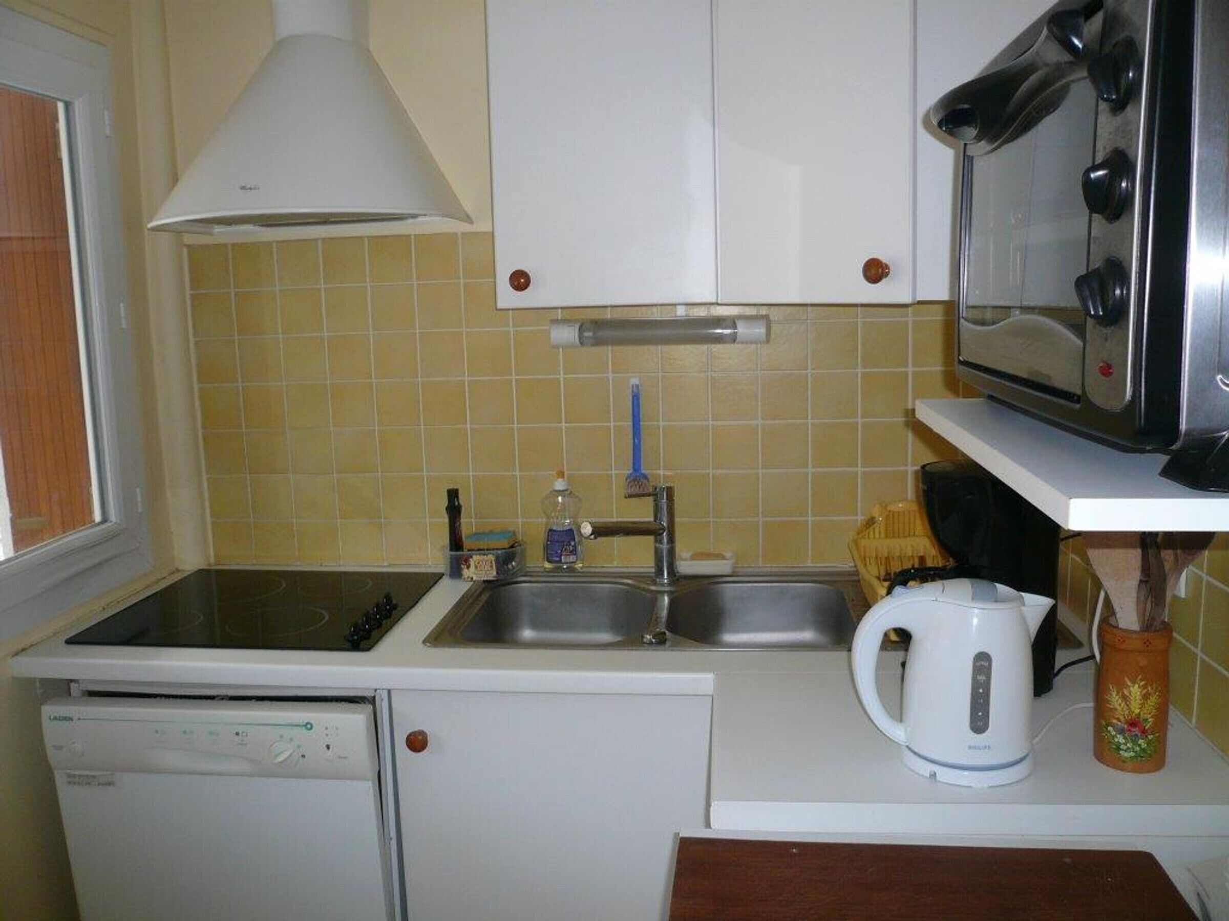 Een kleine keuken met een vaatwasser, spoelbak, magnetron en waterkoker.