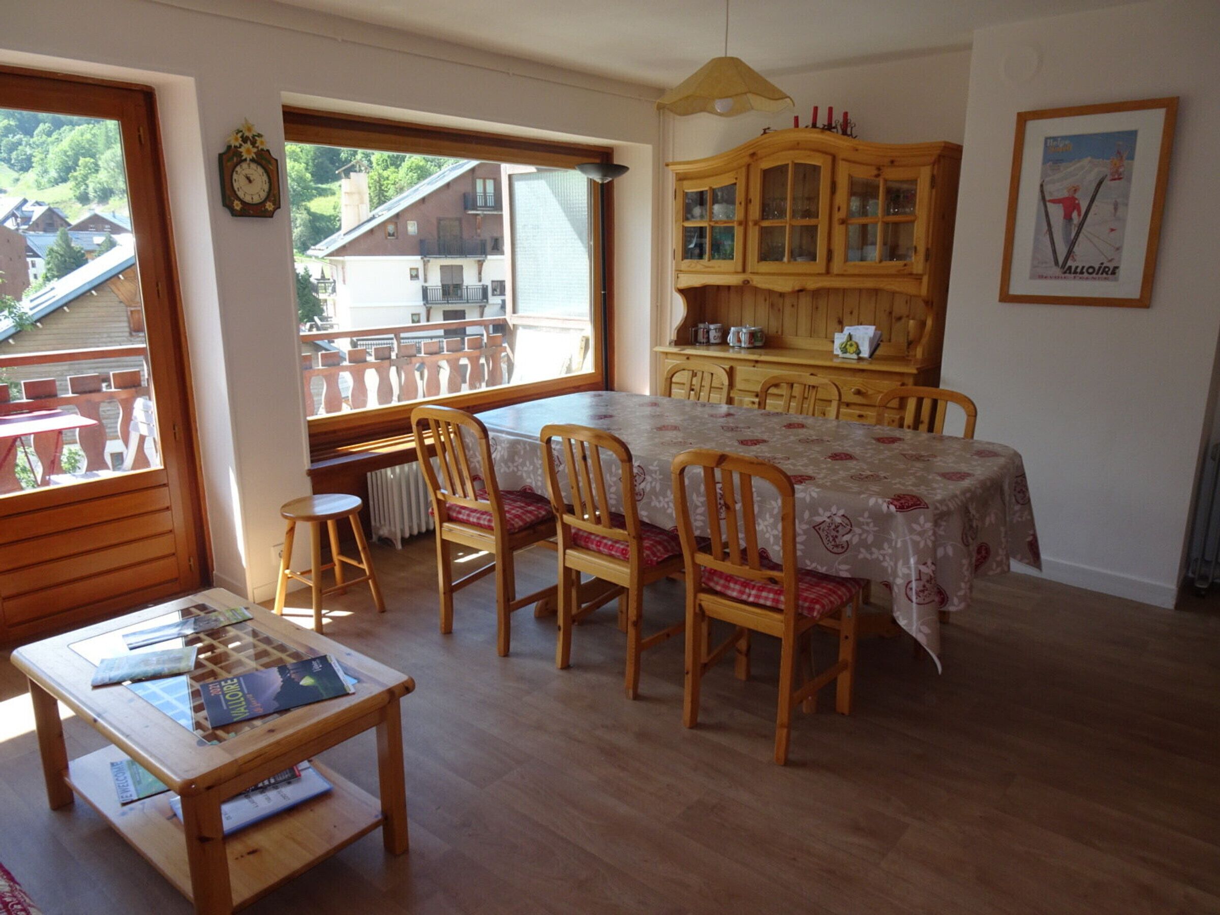 Ein Essbereich mit Holztisch und -stühlen, einem Holzschrank und Blick auf einen Balkon mit Geländer.