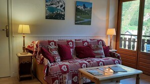 Ein gemütliches Wohnzimmer mit einem gemusterten Sofa, einem Holztisch und zwei an der Wand hängenden Berglandschaften.
