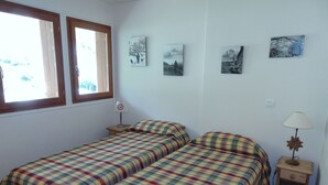 Ein Zimmer mit zwei Betten, einem Fenster und Wandbildern.