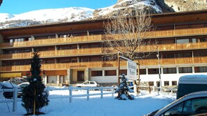 Ein mehrstöckiges Hotel mit Balkonen, einem verschneiten Parkplatz und einem Berg im Hintergrund.
