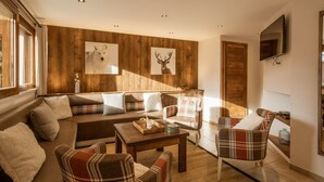 A cozy living room with a sofa set, plaid chairs, a coffee table, and wooden paneling on the walls.