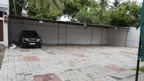 A paved parking area with a black car parked under a covered structure. - Hotel Jayaram (Chidambaram)
