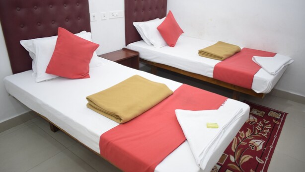 Two single beds with red and white bedding, a brown headboard, and a red patterned rug. - Hotel Jayaram (Chidambaram)