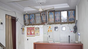 A reception area with a wooden desk, a ceiling fan, and religious paintings on the wall. - Hotel Jayaram (Chidambaram)