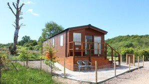 A wooden cabin with a porch, two chairs, and a fenced garden area. - Mountain View - luxury cabin with spectacular alpine and loch views (Taynuilt)