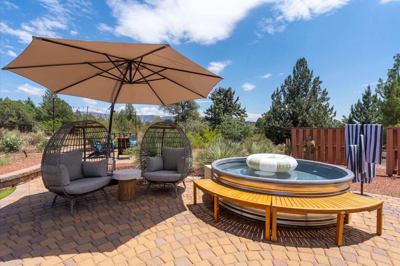A patio area with a hot tub, two wicker chairs, a table, and a large umbrella.