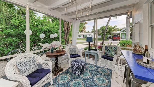 A covered outdoor seating area with wicker furniture, a small table, and a patterned rug. - Blue Egret: Pool, Enclosed Lanai, Close to the Beach by Anna Maria Life Vacation Rentals (Holmes Beach)