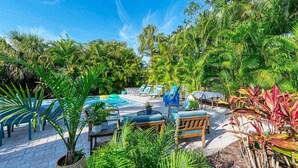 A pool area with lounge chairs and tables, surrounded by lush greenery. - Blue Egret: Pool, Enclosed Lanai, Close to the Beach by Anna Maria Life Vacation Rentals (Holmes Beach)