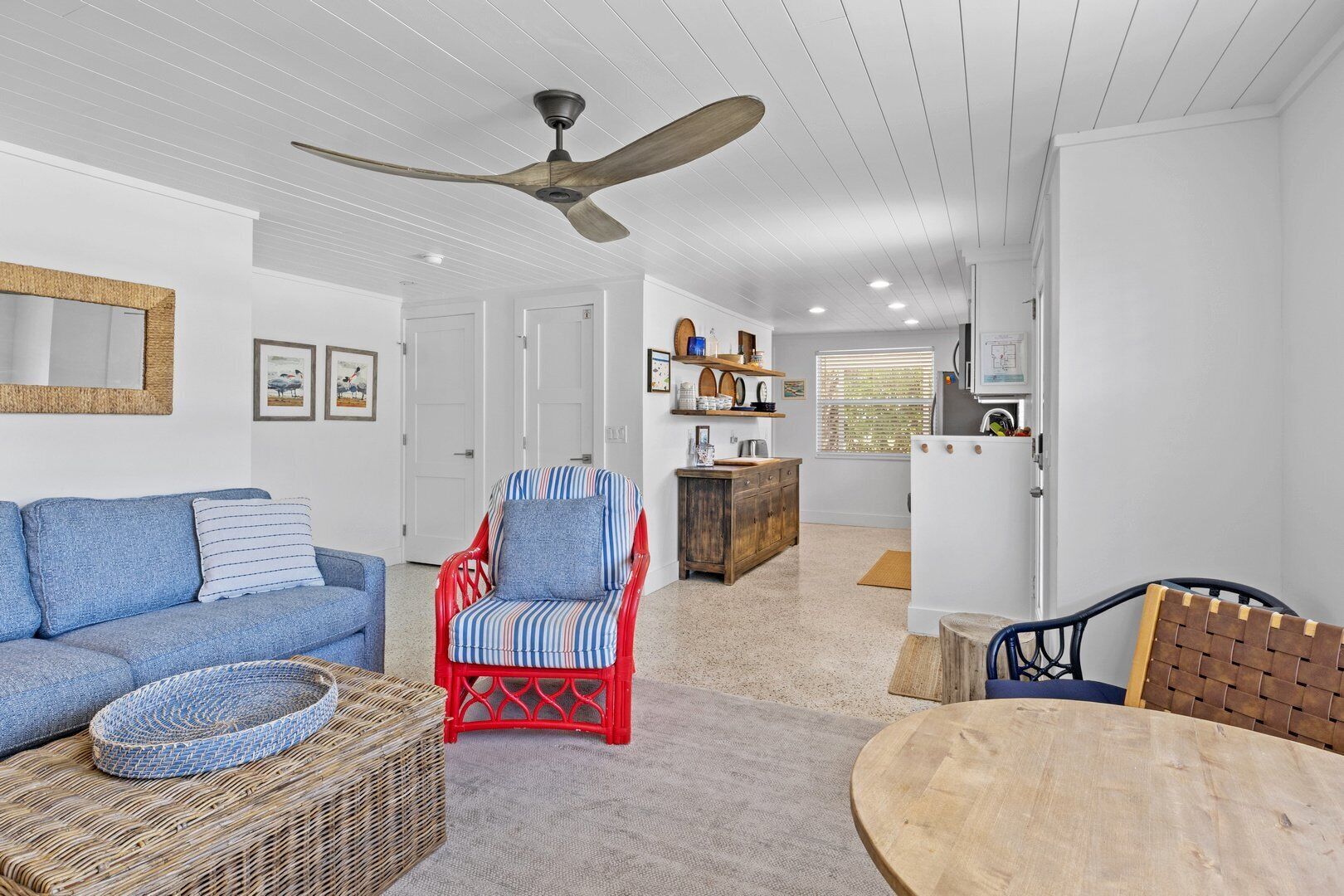 A spacious living room with a blue sofa, a red chair, a wooden table, and a ceiling fan.
