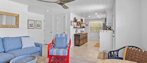 A spacious living room with a blue sofa, a red chair, a wooden table, and a ceiling fan.