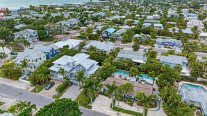An aerial view of a coastal residential area with houses, palm trees, and a beach in the background. - Blue Pelican: Sparkling Pool, Patio Dining, Close to the Beach by Anna Maria Life Vacation Rentals (Holmes Beach)