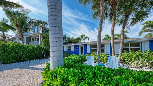 A beachfront property with a blue building, palm trees, and a well-maintained garden. - Blue Pelican: Sparkling Pool, Patio Dining, Close to the Beach by Anna Maria Life Vacation Rentals (Holmes Beach)