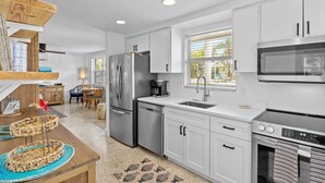 A modern kitchen with white cabinets, stainless steel appliances, and a large window providing natural light. - Blue Pelican: Sparkling Pool, Patio Dining, Close to the Beach by Anna Maria Life Vacation Rentals (Holmes Beach)