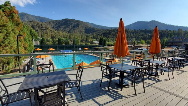Une terrasse avec des tables et des chaises donnant sur une piscine et un paysage montagneux.