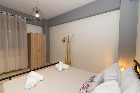 A bedroom with a bed, towels, a wardrobe, a hat stand, and a geometric light fixture.
