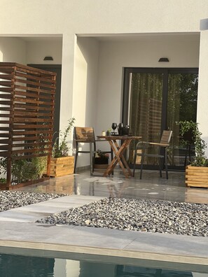 A modern outdoor patio with a pool, wooden furniture, and potted plants.