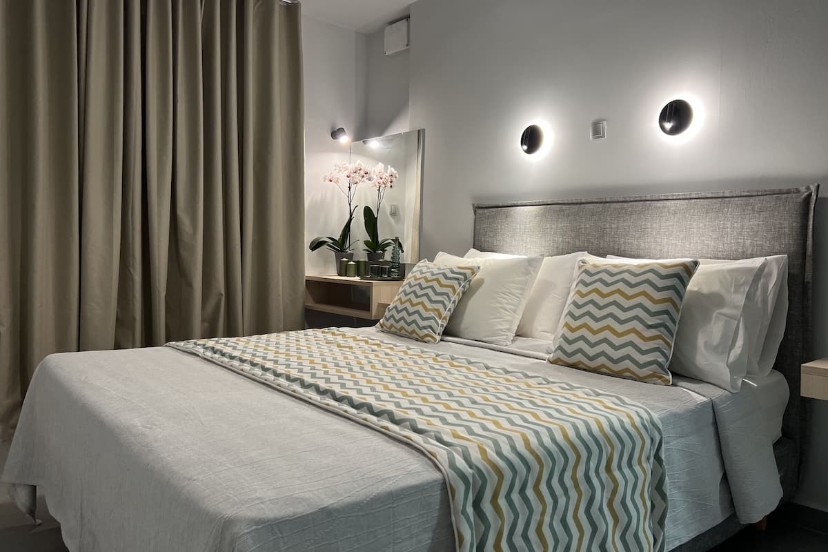 Un dormitorio moderno con una cama grande, una mesita de noche, un espejo y un aplique en la pared.