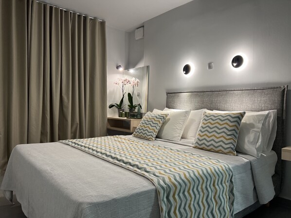 A modern bedroom with a large bed, a nightstand, a mirror, and a wall-mounted light fixture.
