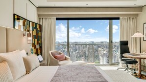 Een moderne hotelkamer met een groot bed, een bureau, een stoel en uitzicht op de stad door een groot raam.