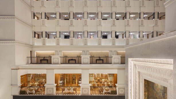 Een hotelinterieur met meerdere verdiepingen, een statige trap, diverse balkons en een luxe eetgedeelte.