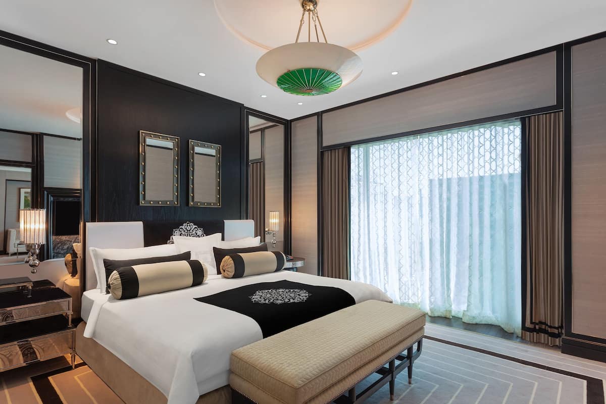 Ein modernes Hotelzimmer mit einem großen Bett, Nachttischen, einer Bank und einem großen Fenster mit Vorhängen.