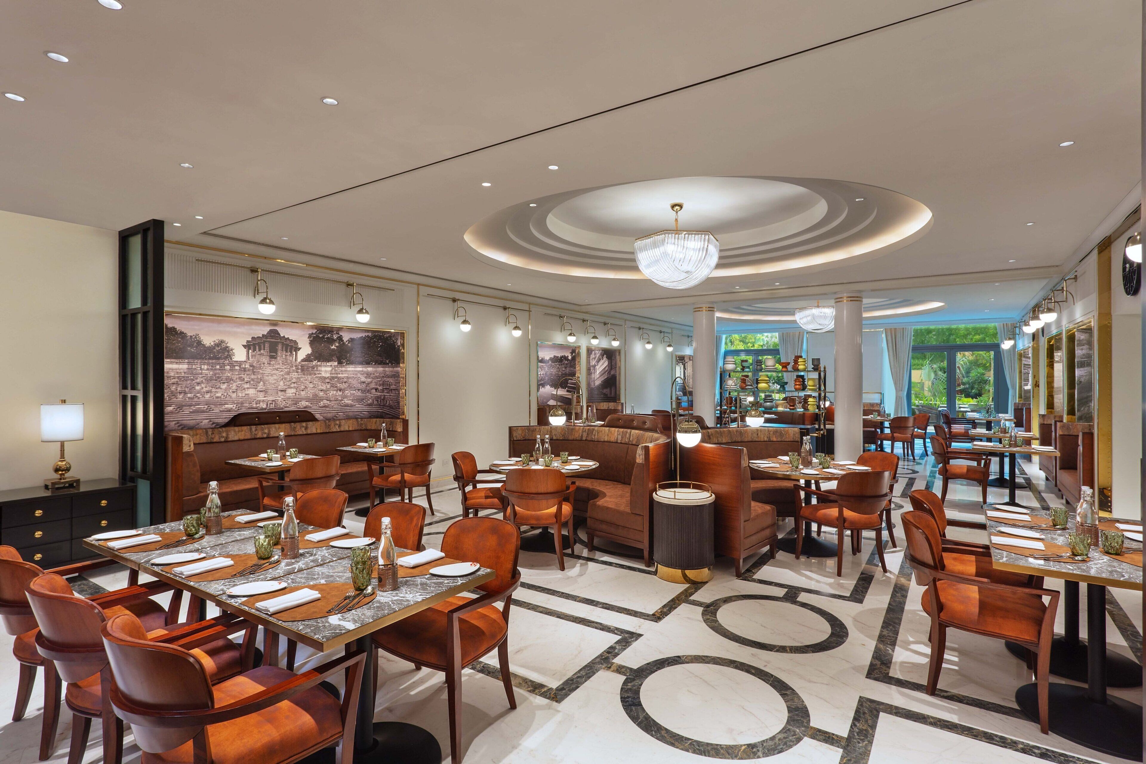A spacious hotel lobby with multiple dining areas, a bar, and a large mural on the wall.