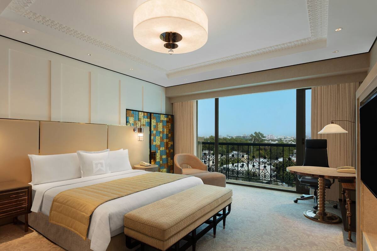 Ein Hotelzimmer mit einem großen Bett, einem Schreibtisch mit Stuhl, einem Balkon mit Blick und einem Fernseher.