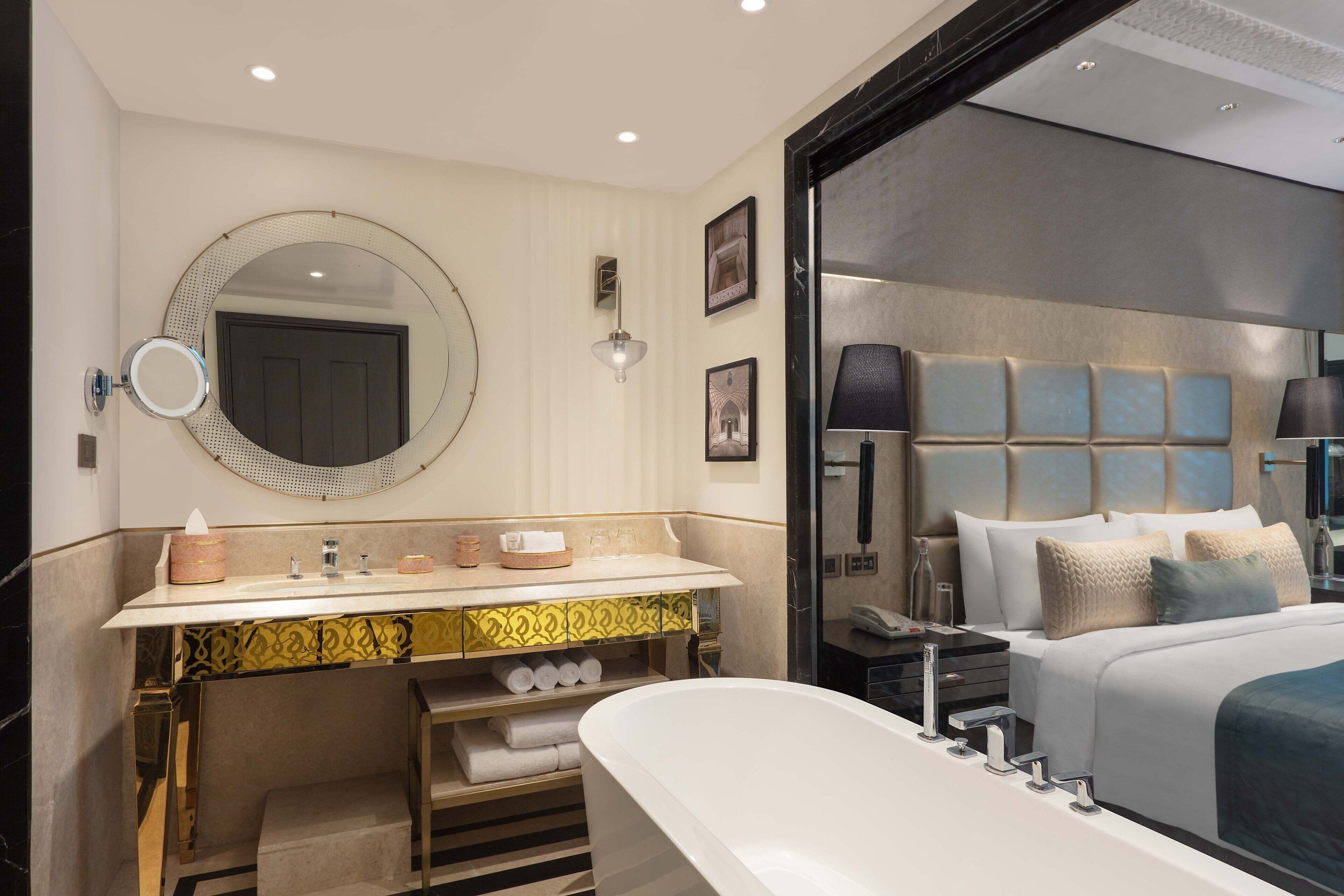 A modern bathroom with a freestanding bathtub, a vanity with a mirror, and a large bed with a headboard.