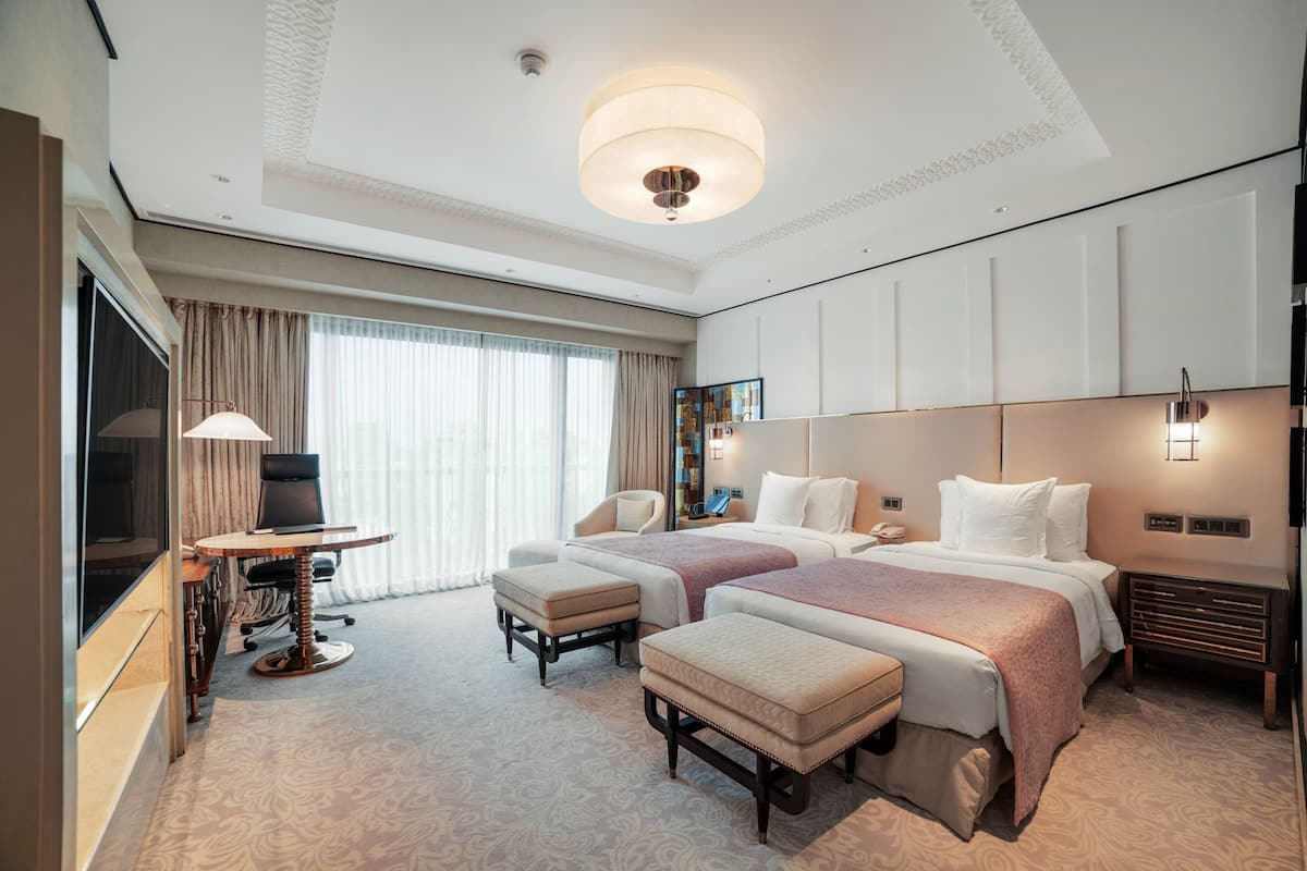 Ein Hotelzimmer mit zwei Betten, einem Schreibtisch, einem Stuhl und einem Fernseher.