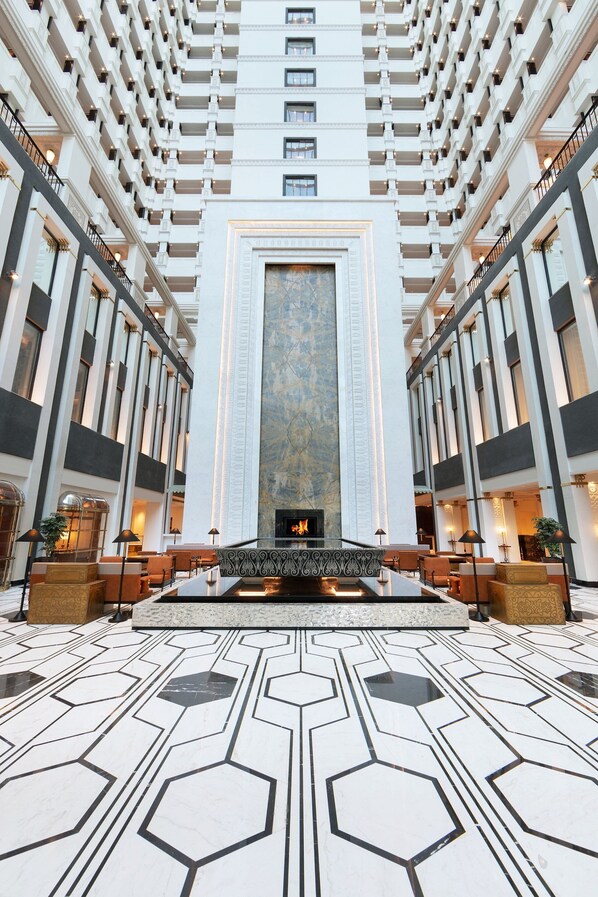 Un vestíbulo de hotel con chimenea central, techos altos y un diseño geométrico en el suelo.