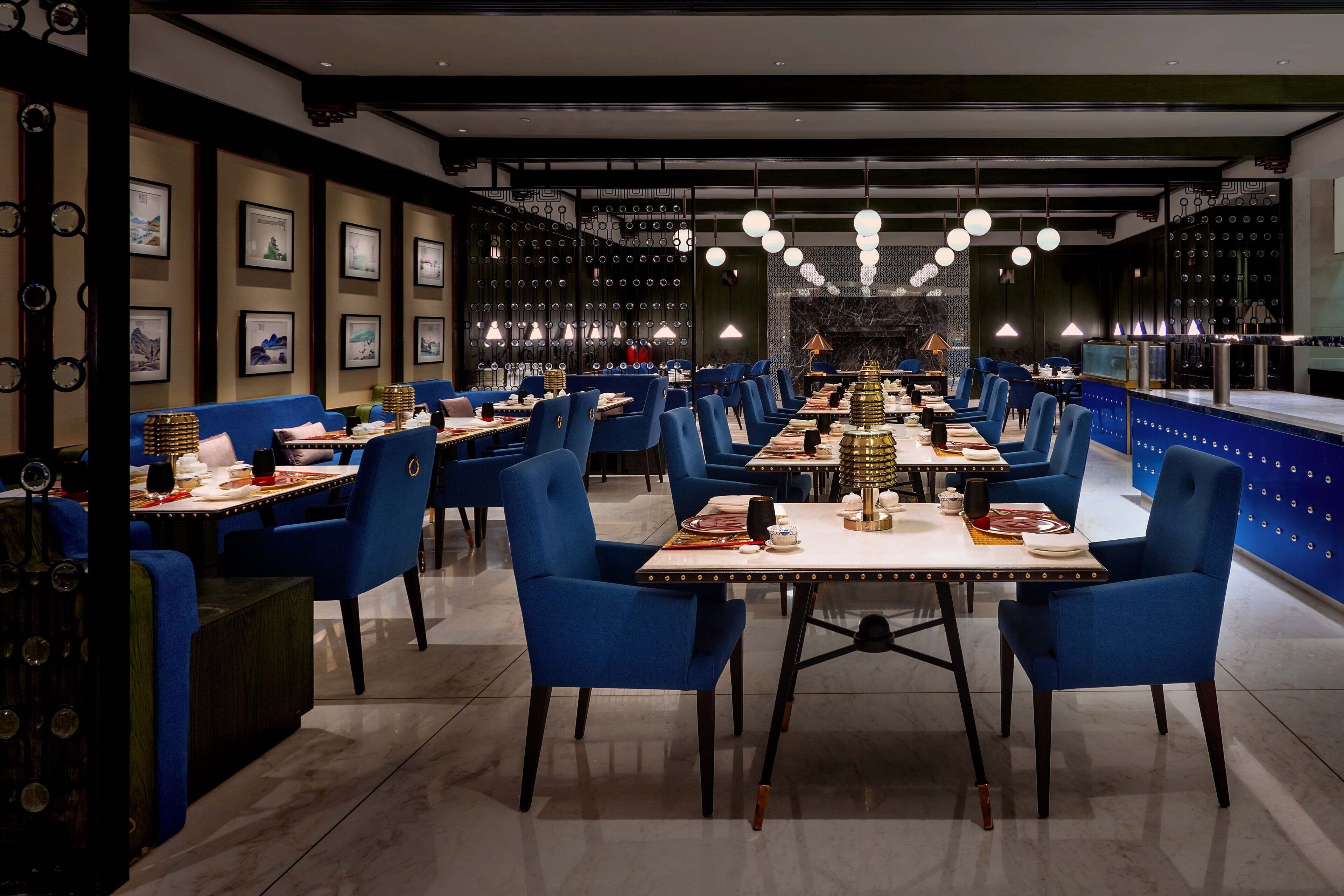 Un restaurante moderno con sillas y mesas azules, obras de arte enmarcadas en las paredes e iluminación colgante.