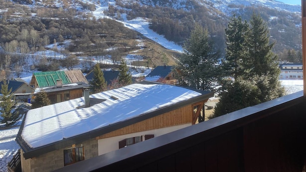 A mountain landscape with snow-covered slopes and a view of a building with a wooden facade and a green roof. - Studio cabin 3 people east-facing with balcony (Valloire)
