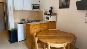 A compact kitchen with white cabinets, a microwave, and a sink. There's a wooden table with chairs, a small trash bin, and a wall-mounted TV. - Studio cabin 3 people east-facing with balcony (Valloire)