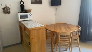 A compact living space with a wooden dining table and chairs, a microwave, a television, and a wall-mounted clock. - Studio cabin 3 people east-facing with balcony (Valloire)