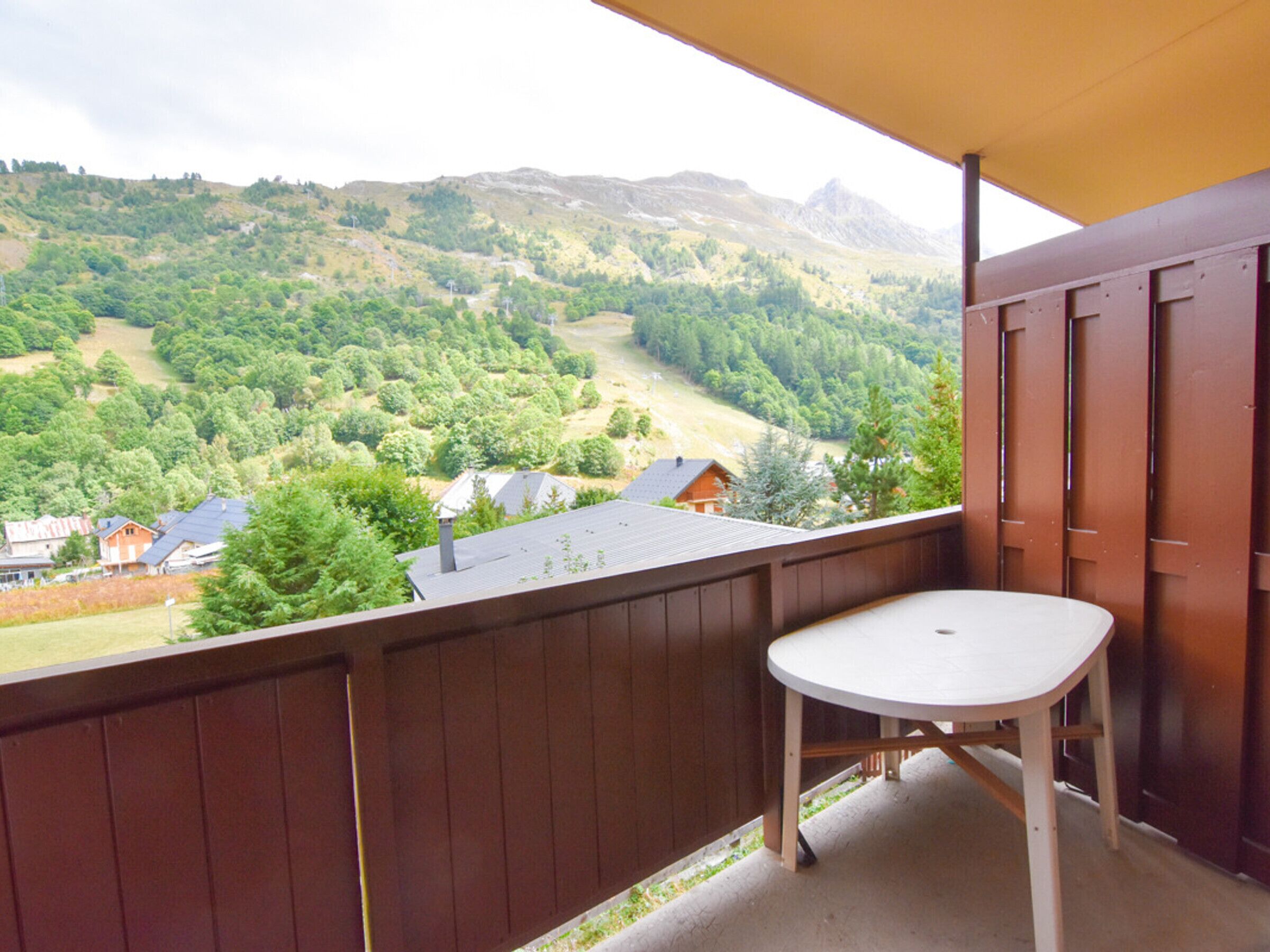 A balcony with a view of a mountainous landscape, a wooden railing, and a white table.