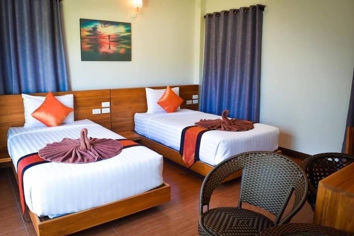 Habitación de hotel con dos camas individuales, cabecera de madera, un cuadro en la pared y sillas de mimbre.
