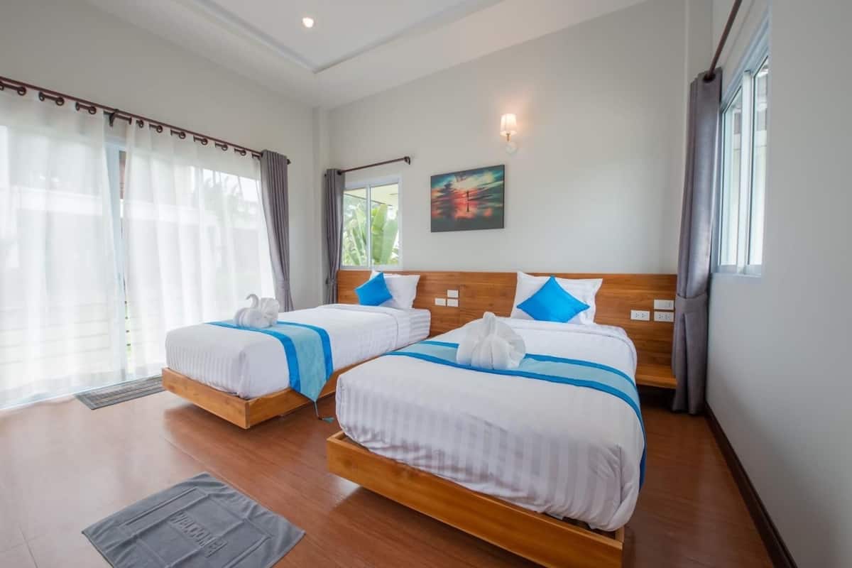 Habitación de hotel con dos camas, cabecero de madera, un cuadro en la pared y una ventana con cortinas.