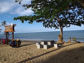 Una platja amb un senyal de fusta, blocs de formigó i un arbre.