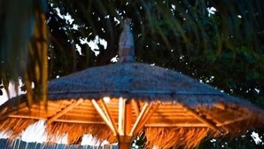 Una sombrilla con techo de paja, dos sillones de playa y una arena con vista al mar.