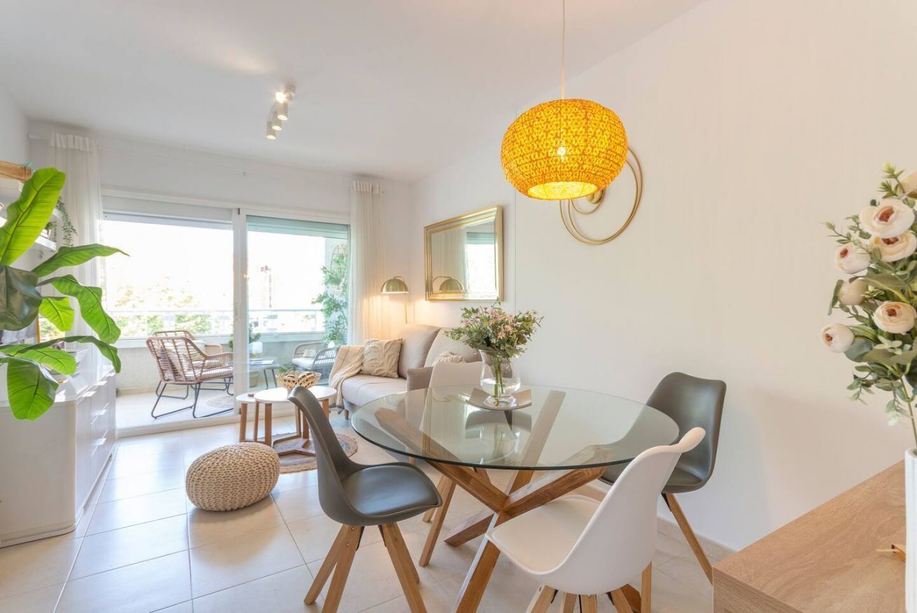 Un espace repas moderne avec une table en verre, des chaises en cuir et un luminaire suspendu jaune.