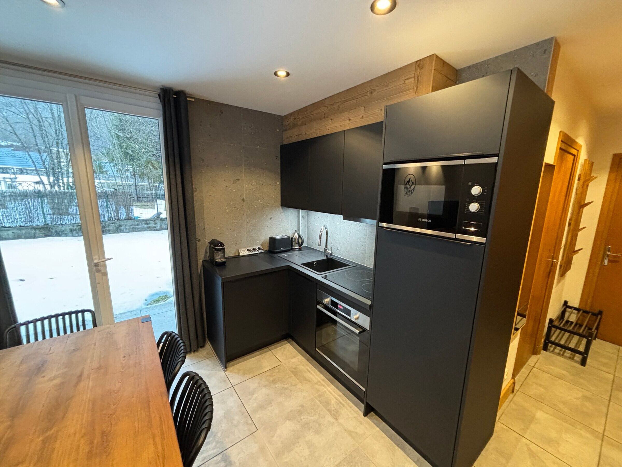 Una cocina compacta con un refrigerador Bosch, un horno empotrado y una cafetera.
